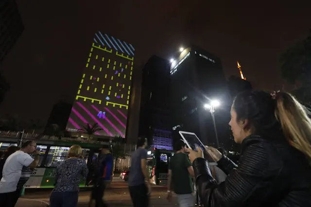 Fachada de edifício na Avenida Paulista mapeada como tela de jogo, com operador segurando tablet